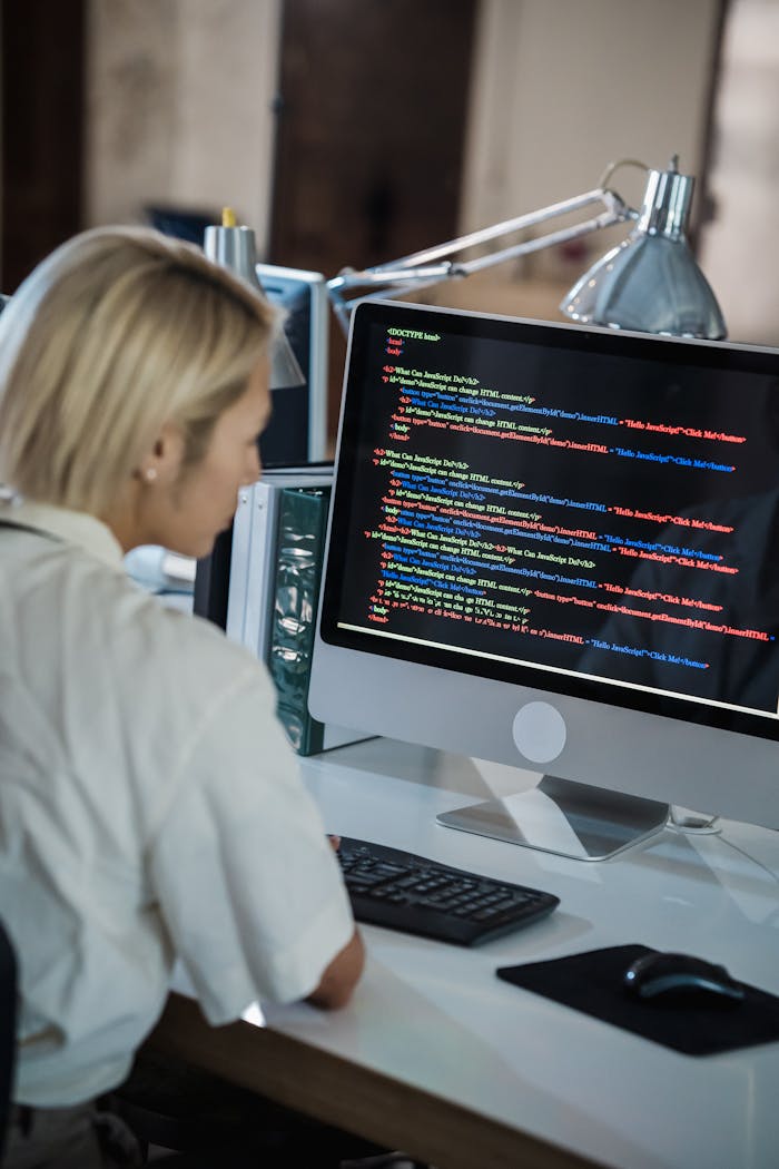 Woman with blonde hair coding on computer in a modern office setting.